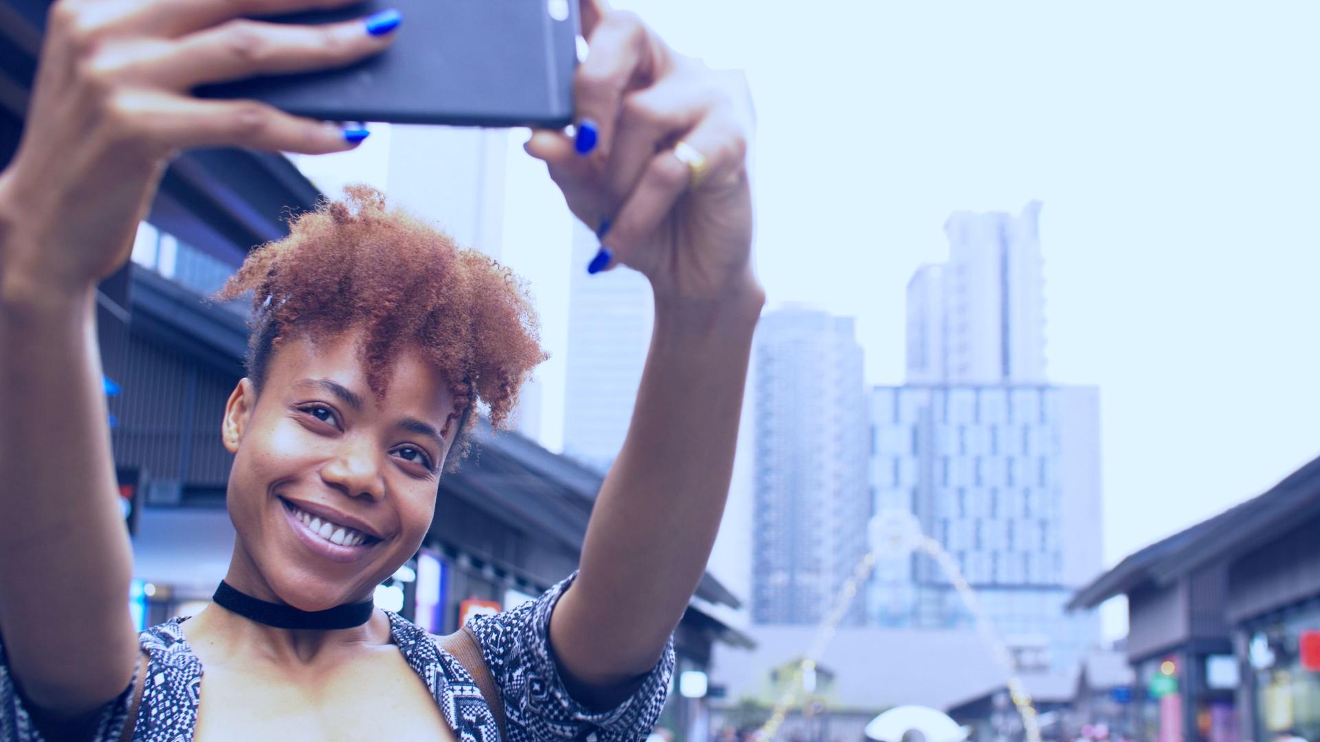 jeune femme africaine heureuse utilisant le téléphone mobile prenant la photo dans la rue