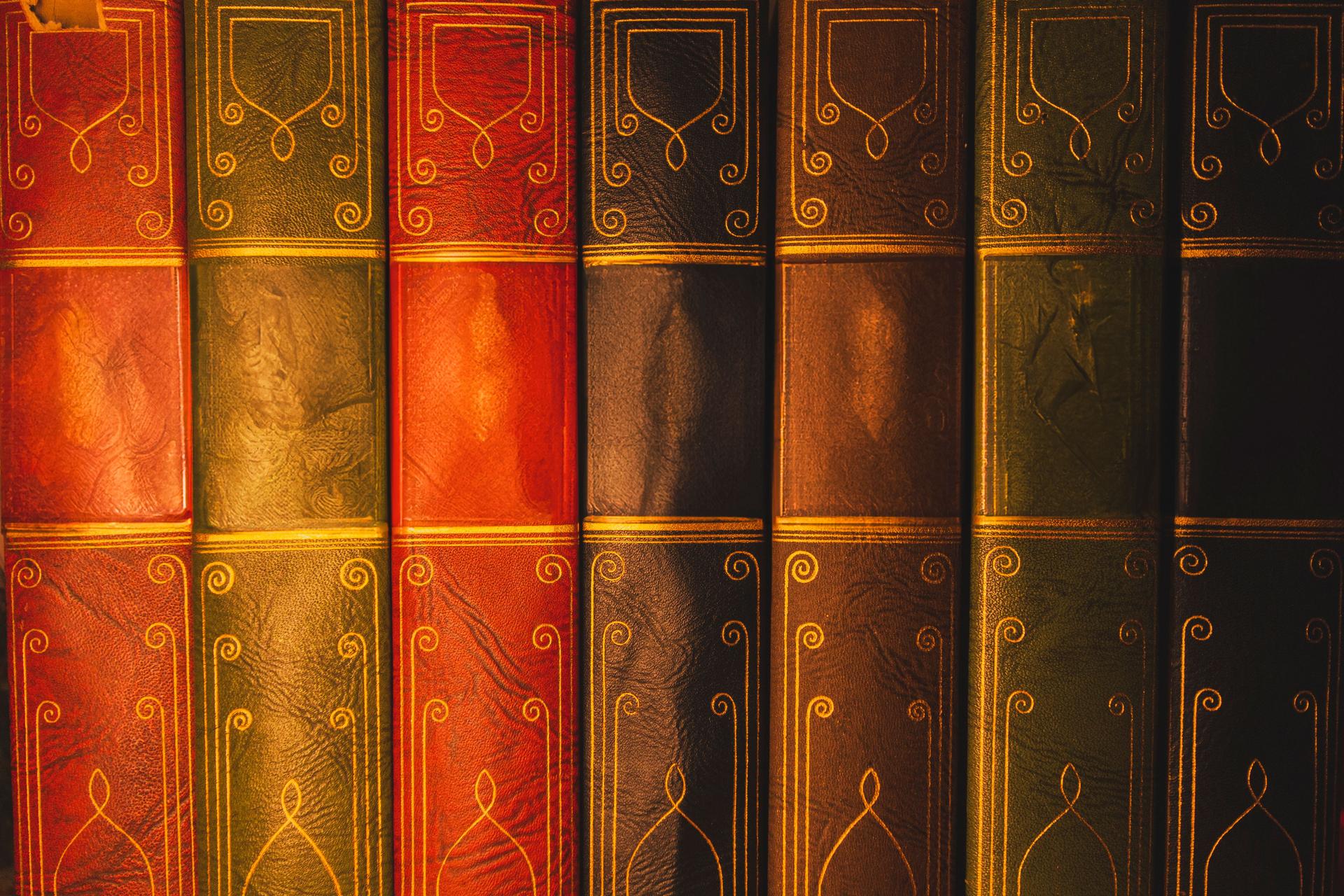 Collection de livres reliés en cuir vintage multicolores, projetés dans une lumière chaude.